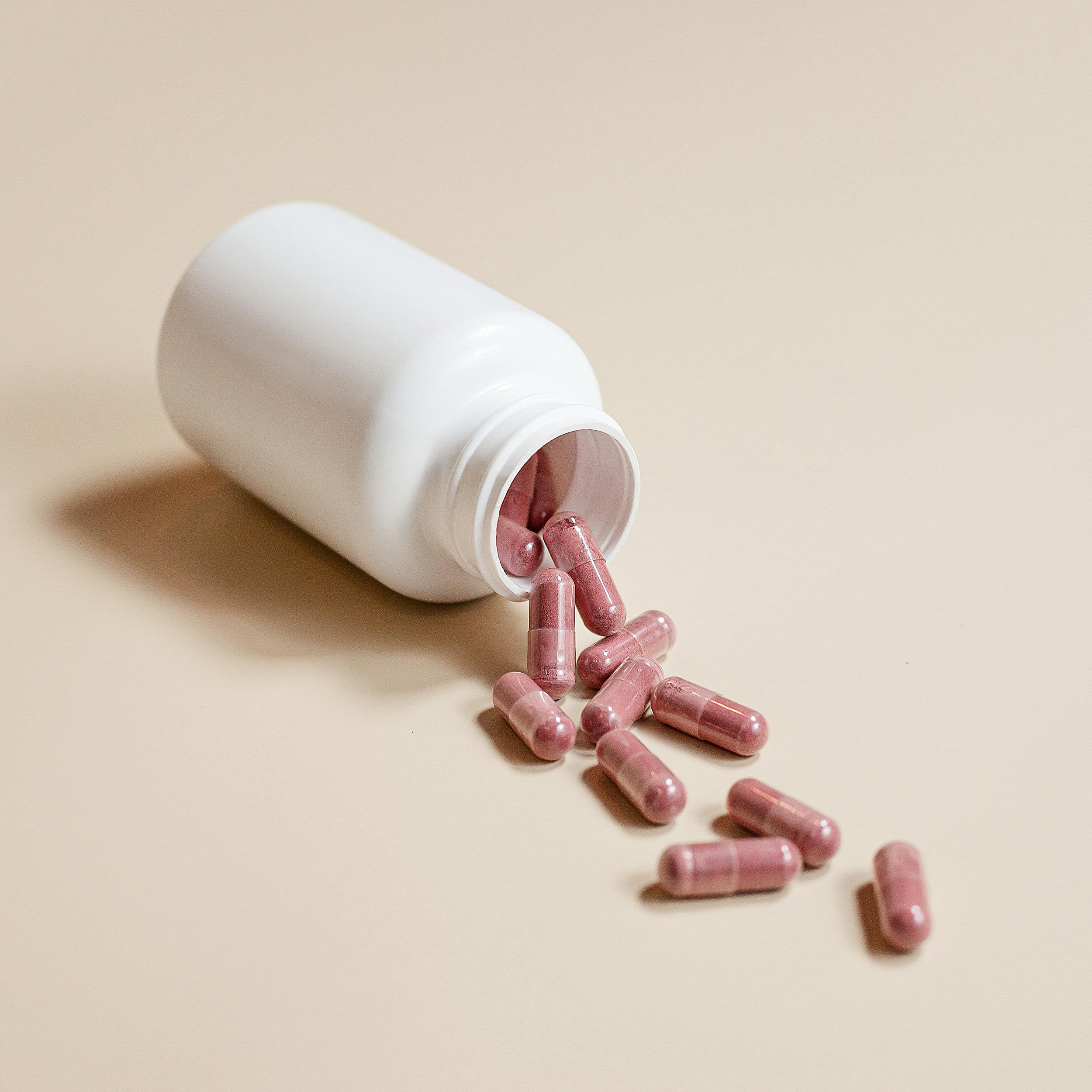 A white bottle spills pink capsules onto a beige surface, ideal for healthcare themes.