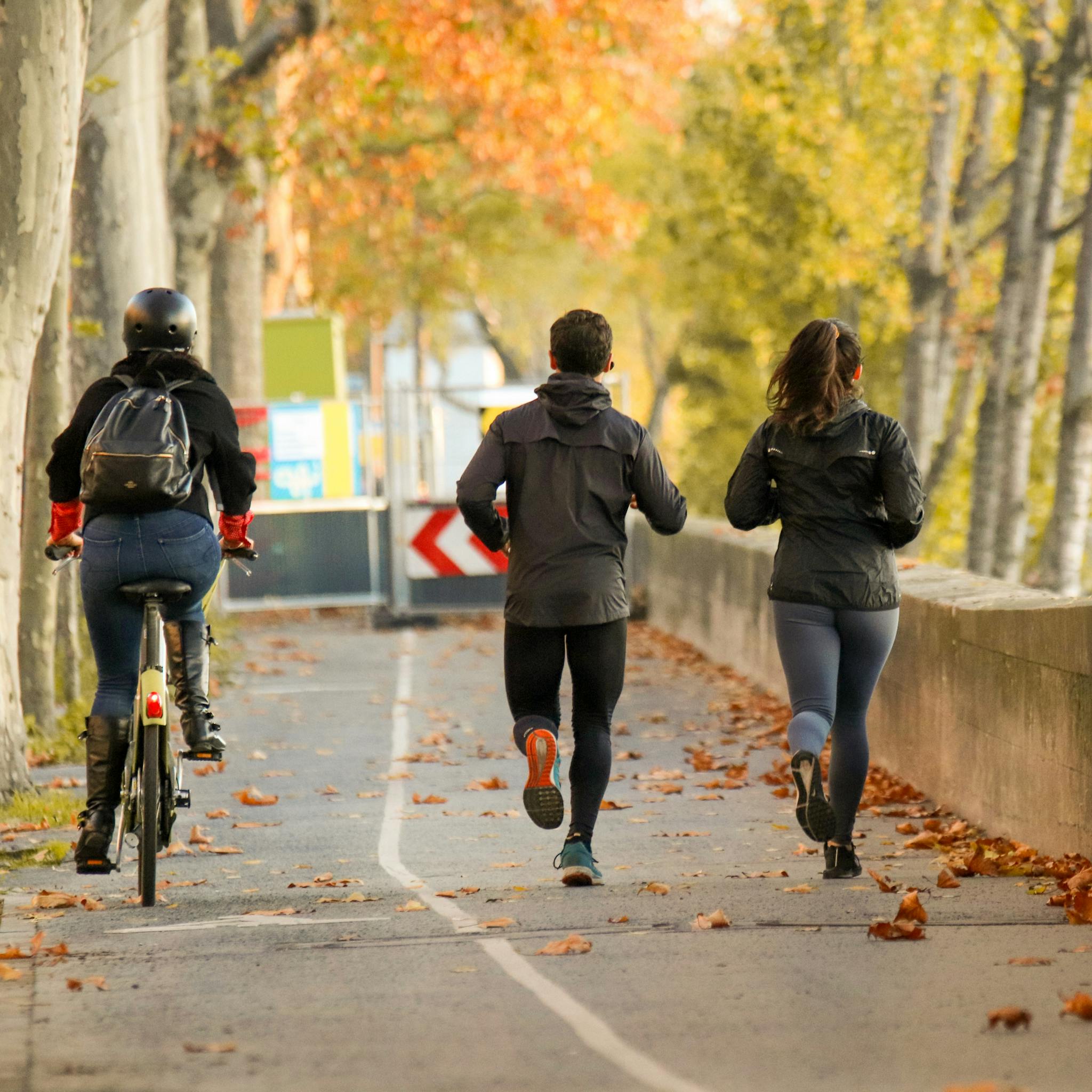 People enjoying outdoor exercise with cycling and running on a leaf-covered path in autumn.