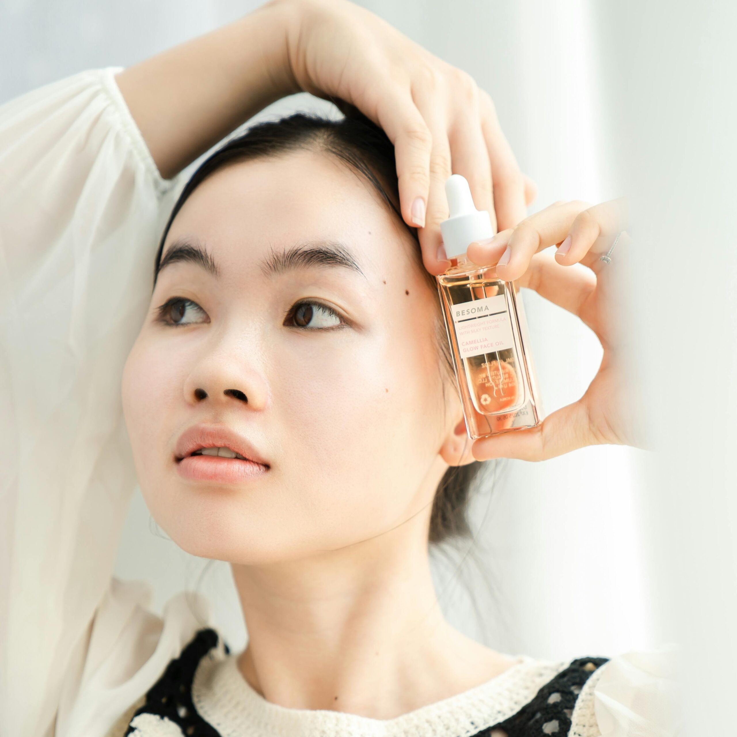 Elegant portrait of an Asian woman presenting Besoma skincare product indoors.