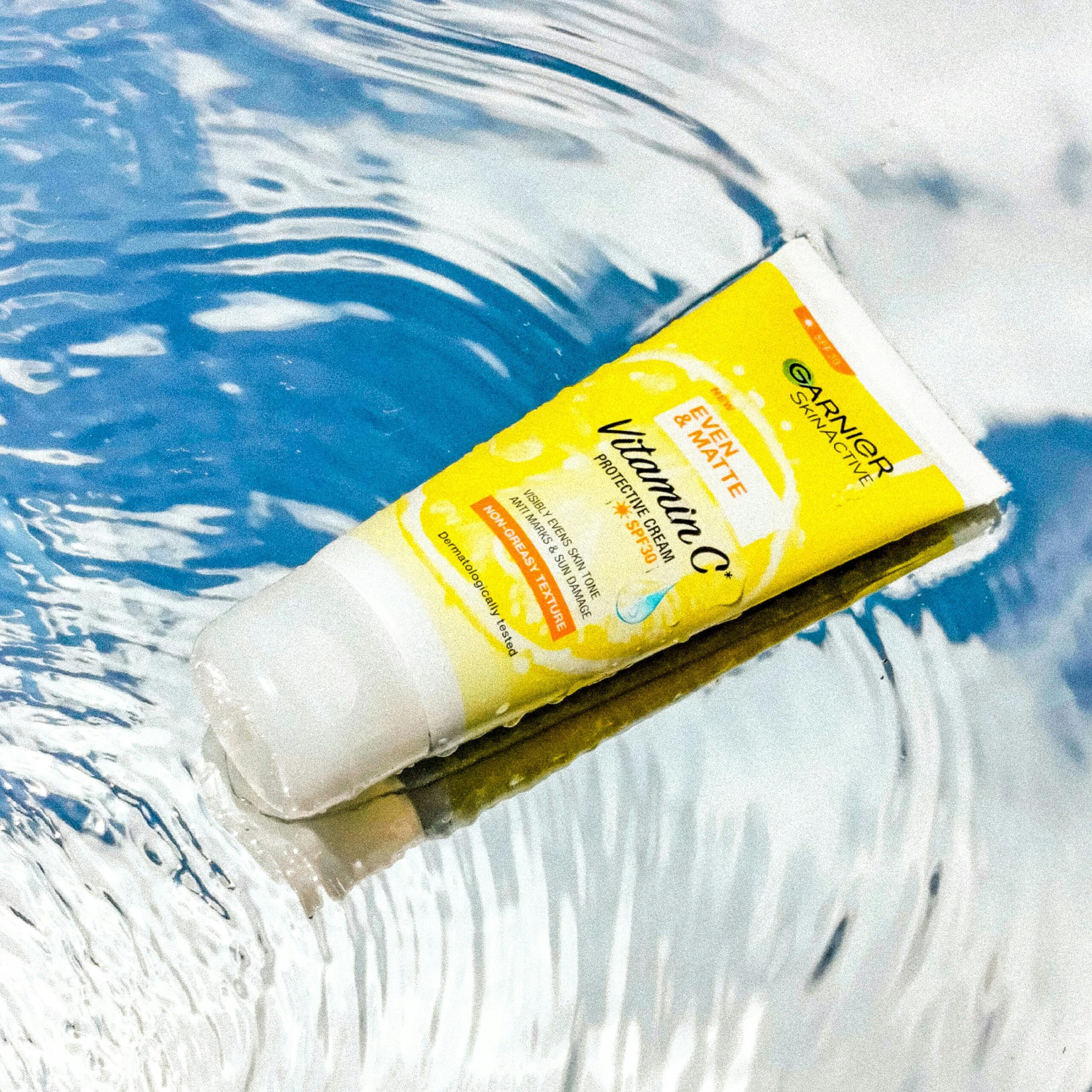 Brightly colored tube of vitamin C protective cream floating on rippling water.