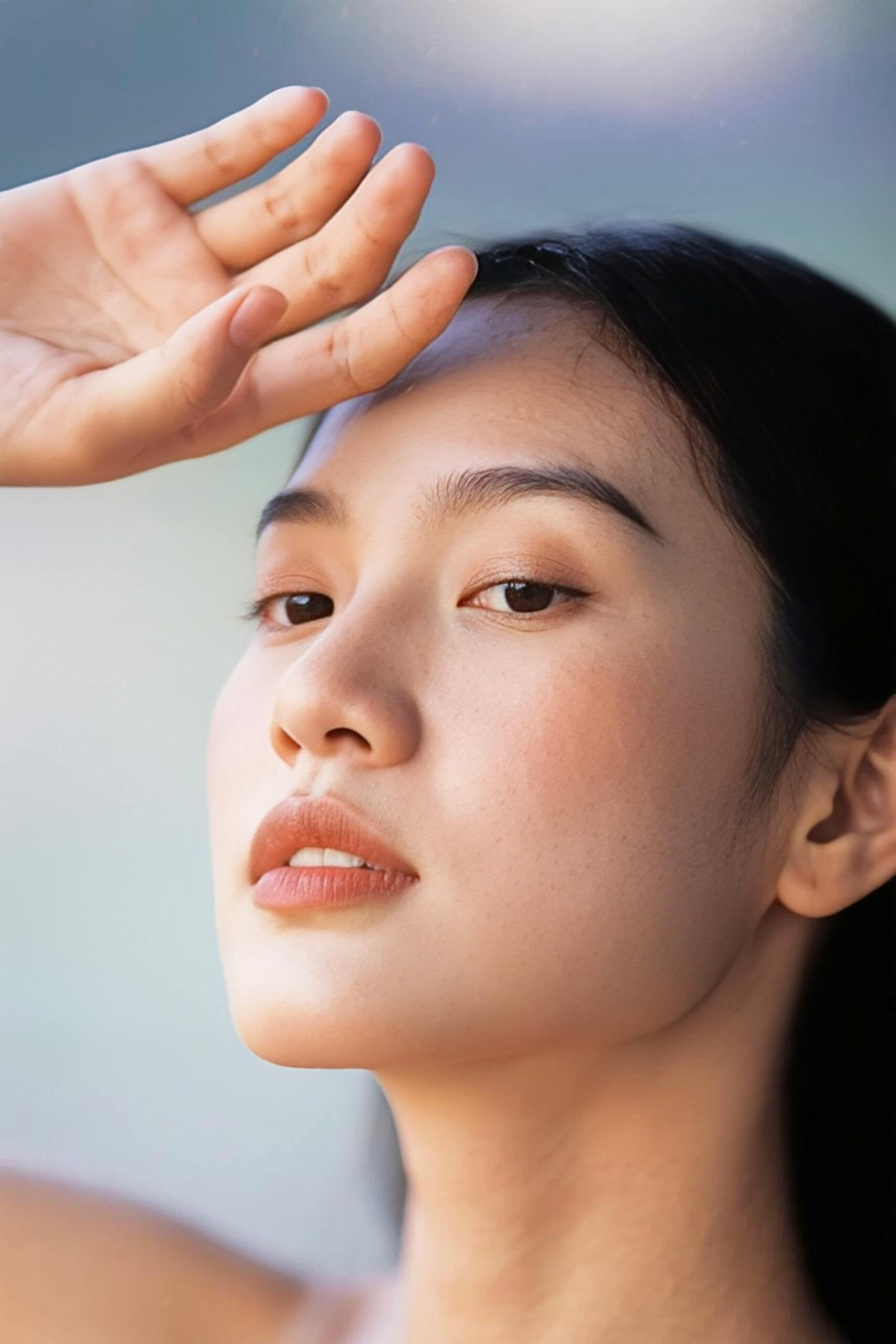 Close-up shot of a young woman shielding her eyes with her hand, showcasing natural beauty.