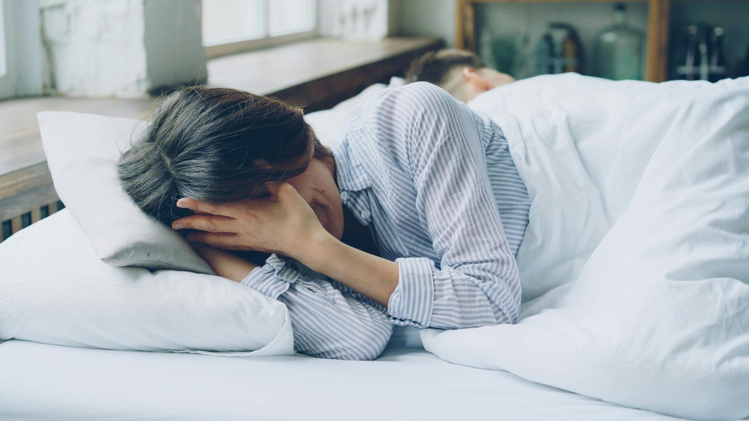 A woman in bed showing signs of anxiety. Soft light indoors.
