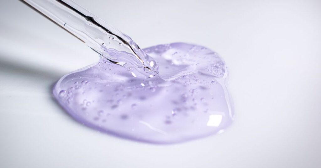 Ingredients A pipette dispensing clear purple cosmetic gel onto a smooth surface.