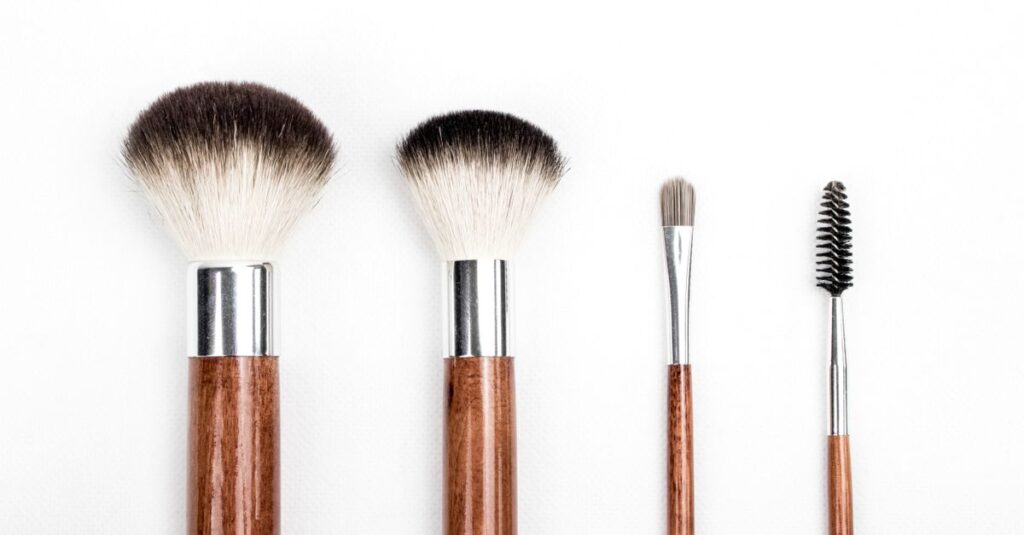 Stylish flat lay of four wooden makeup brushes against a clean white background.