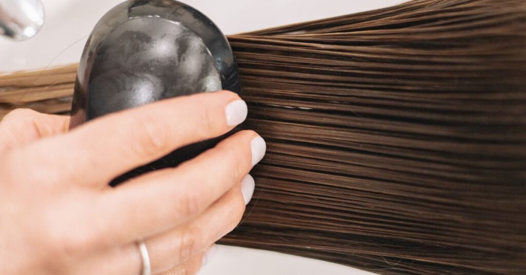 Close-up of a woman brushing long brown hair with a black brush, highlighting hair care and grooming.