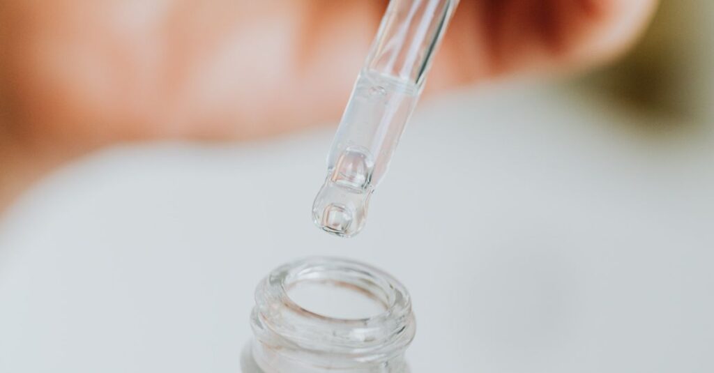 Ingredients Hand holding a dropper, applying serum from a frosted glass bottle, close-up view.