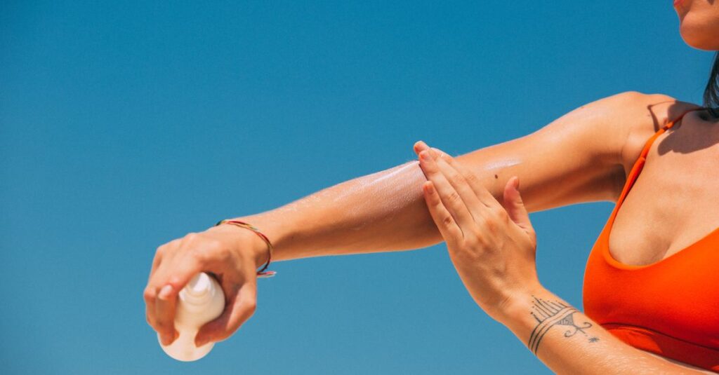 Skincare Close-up of a woman applying sunscreen on her arm under a clear blue sky at the beach.