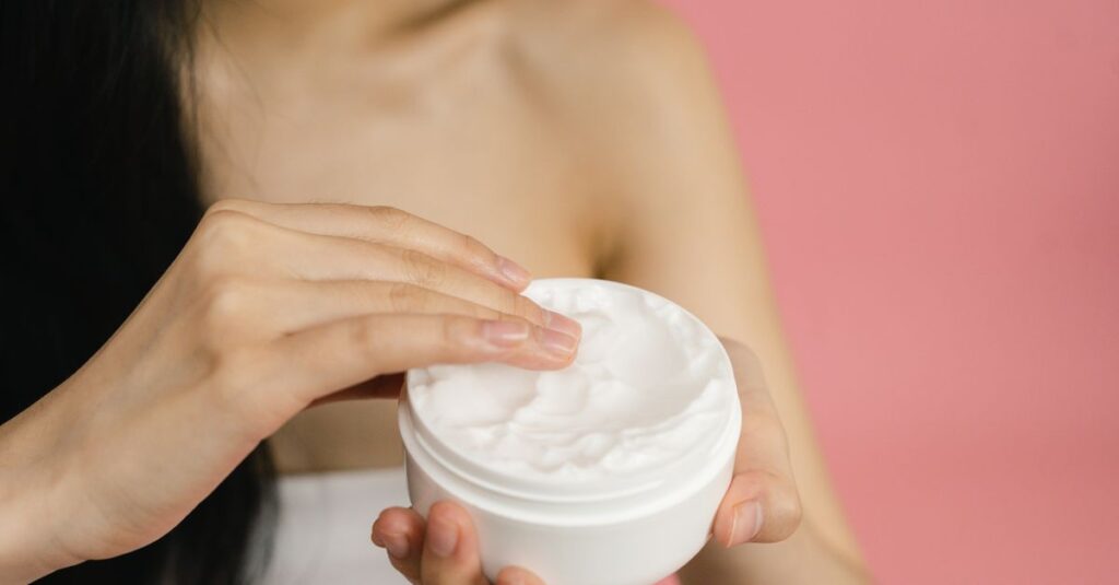 Skincare Close-up of a woman applying white cream from a jar against a pink background.